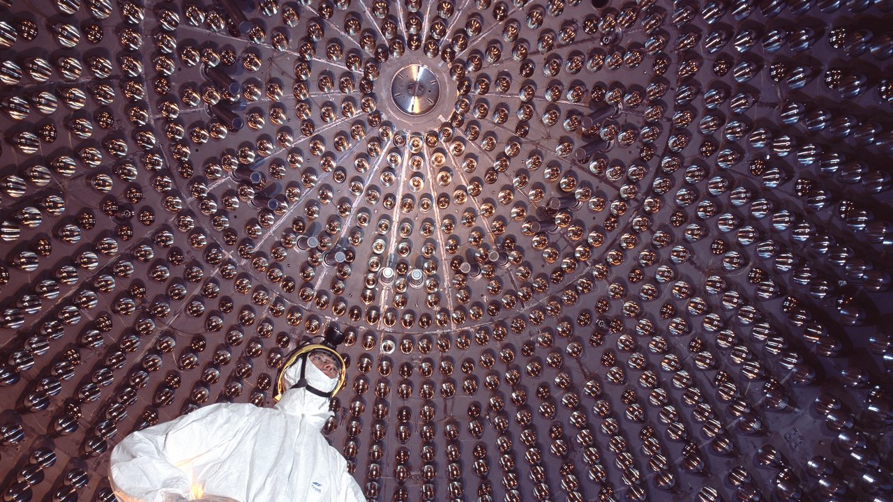 Ein Mensch im weißen Reinraumanzug und Helm in einer an der Wand mit Glaskugeln gespickten Kuppel